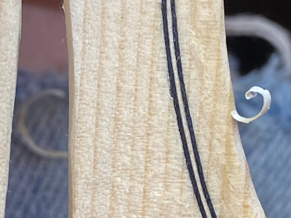 A cutout view of a violin sound hole with purfling. The wood is still in-the-white and there is a curl of wood at the outer edge still attached from carving the edge.